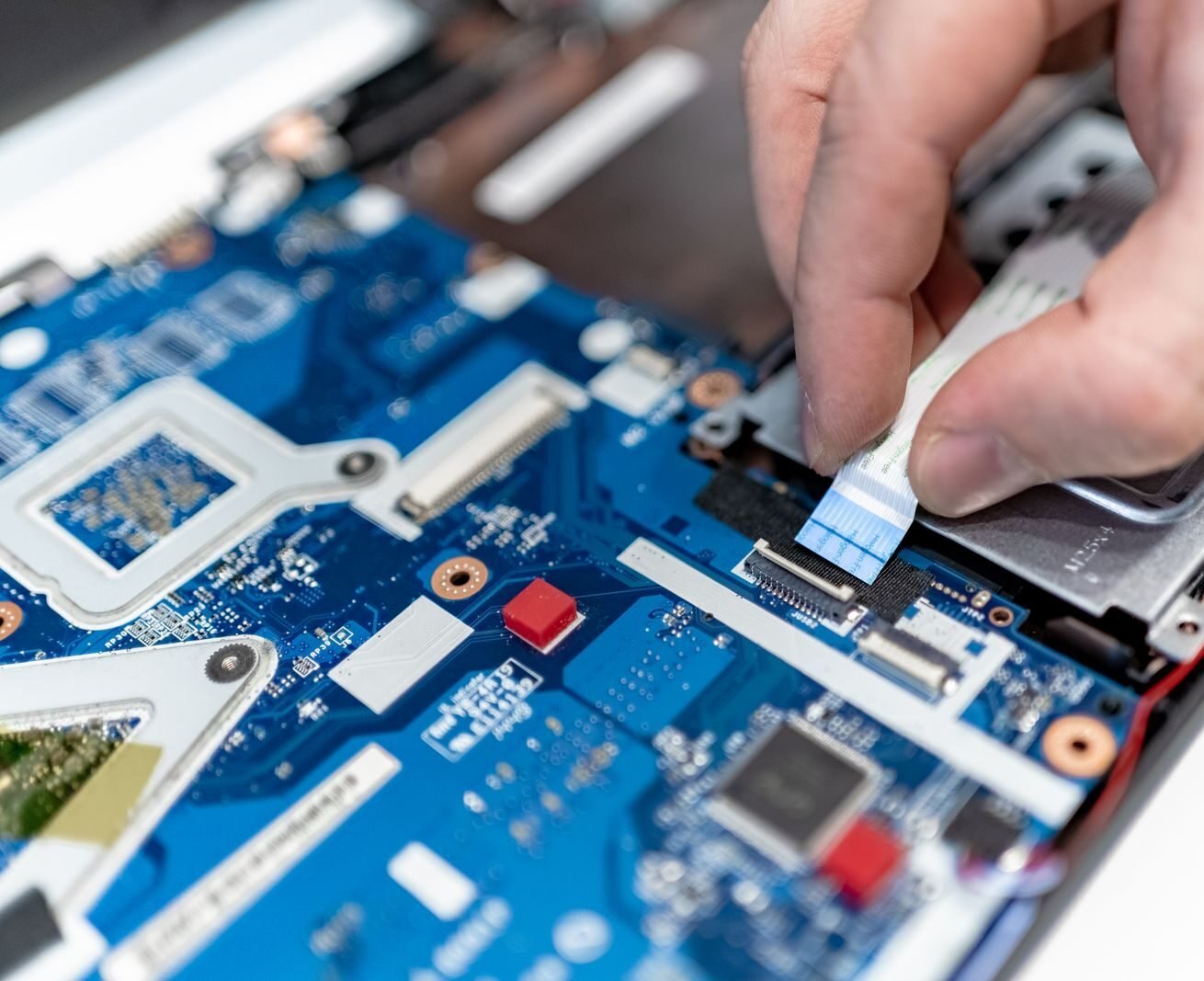 Close-up image of hands repairing a laptop circuit board showing intricate details of electronics.